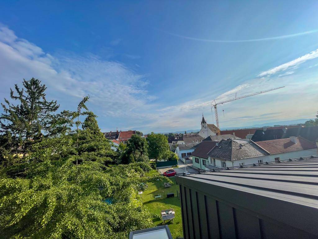 Weitblick über die Dächer der Stadt mit grüner Umgebung und einem Kirchturm im Hintergrund.