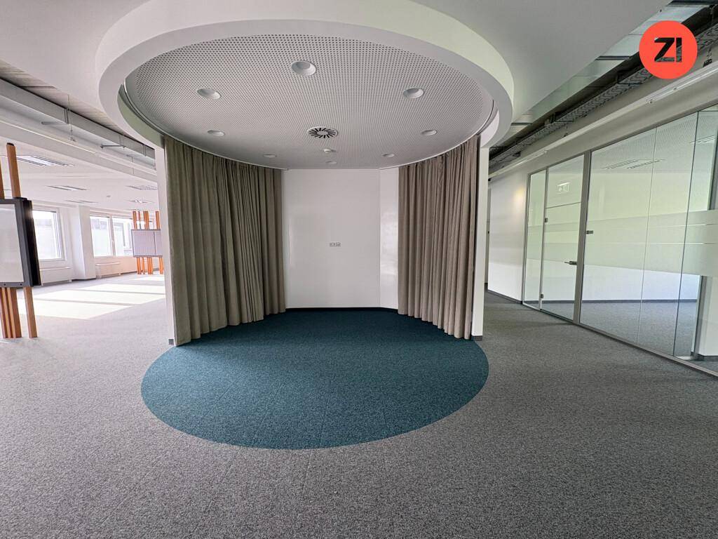 Runder Besprechungsbereich mit blauem Teppich, Vorhängen und indirekter Beleuchtung in einem offenen Büro.