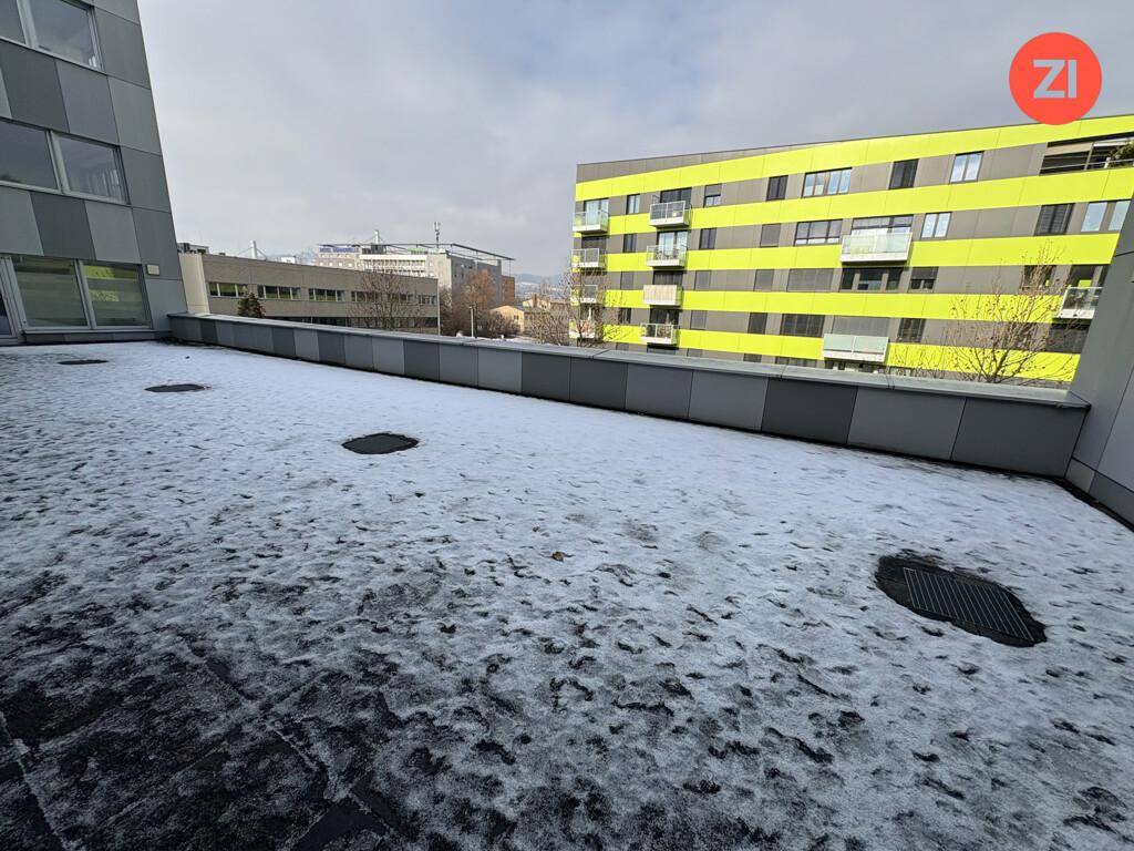 Eine große, schneebedeckte Terrasse mit Blick auf umliegende Gebäude und den Himmel.