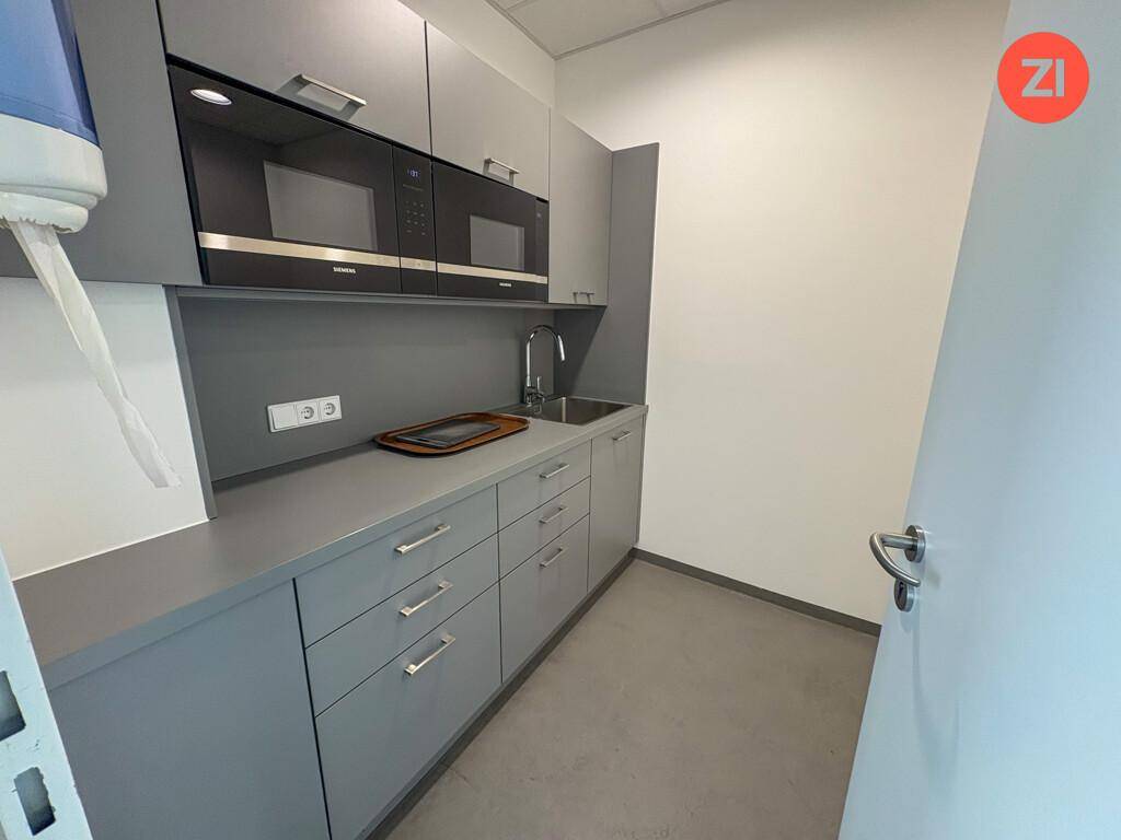 Kleine, moderne Küchenzeile mit grauen Schränken, Spüle und integrierter Mikrowelle und Backofen.