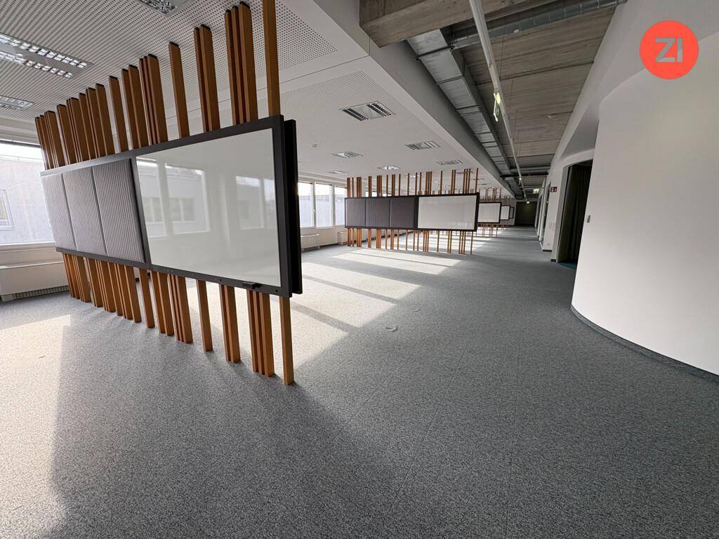 Offener Bürobereich mit modularen Trennwänden aus Holz und Bildschirmen, sowie grauem Teppichboden.