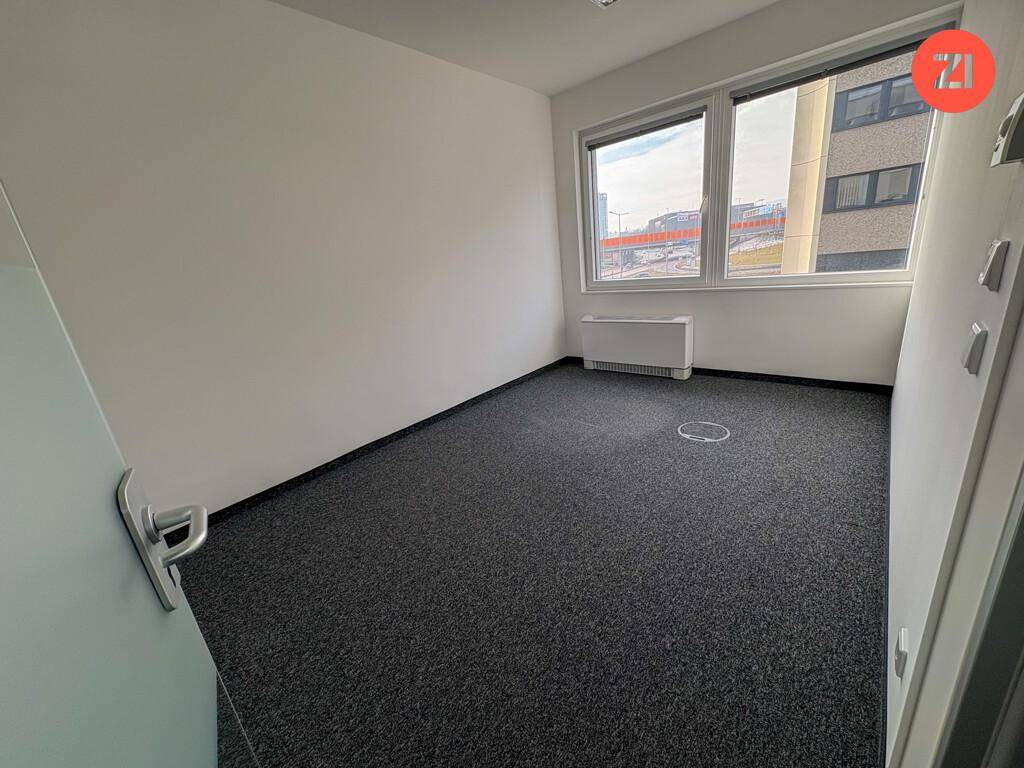 Kleiner, heller Büroraum mit grauem Teppichboden und Fenstern, die einen Blick auf die Straße bieten.