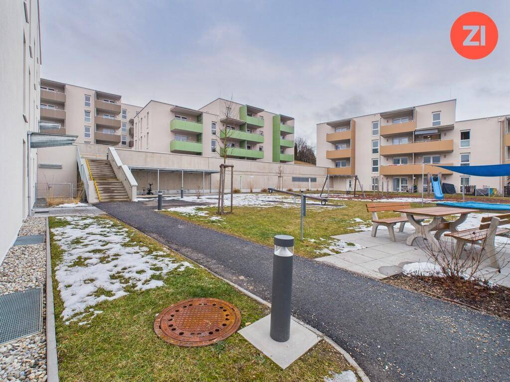 Außenbereich der Wohnanlage mit Spielplatz, Sitzgelegenheiten und gepflegten Grünflächen.