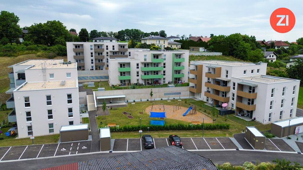Luftaufnahme einer modernen Wohnanlage mit mehreren Gebäuden, Spielplatz und Parkplätzen.