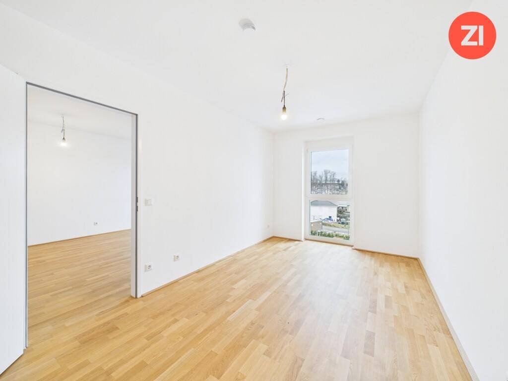 Geräumiges Schlafzimmer mit hellem Parkettboden und einem großen Fenster, das viel Licht hereinlässt.