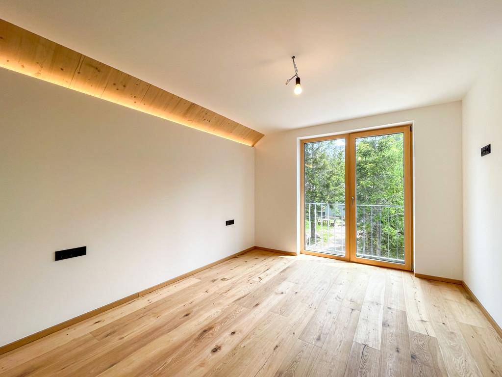Helles Zimmer mit Holzboden und Zugang zu einem französischen Balkon mit Blick ins Grüne.