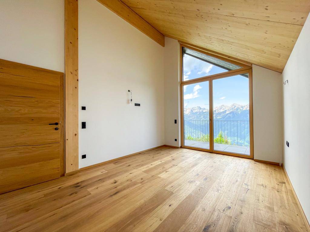 Helles Zimmer mit Holzboden, Dachschräge und großen Fenstern mit beeindruckendem Bergblick.