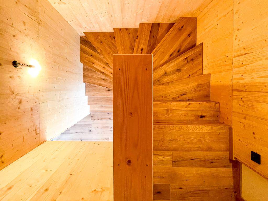 Holztreppe mit Massivholzstufen und Holzverkleidung, die die verschiedenen Ebenen verbindet.
