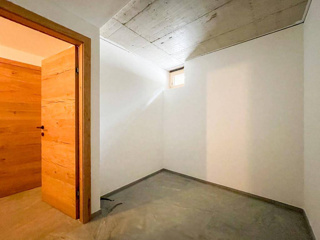 Einfacher Abstellraum mit Betonboden und Holztür, ideal für Lagerzwecke.
