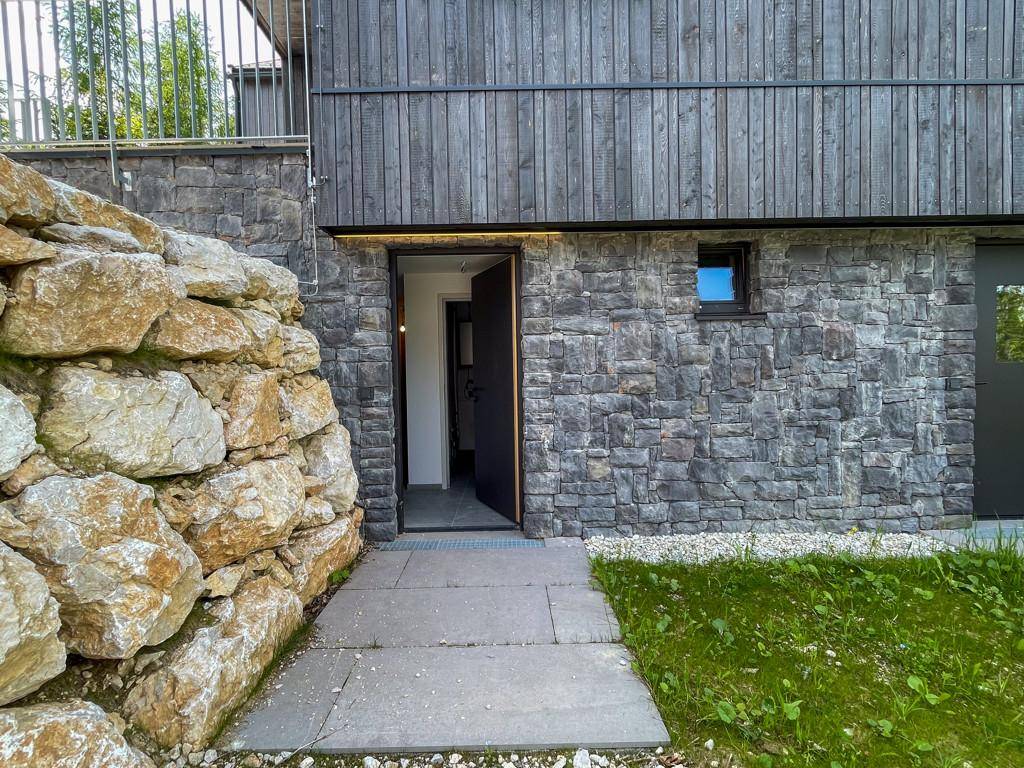 Moderner Gebäudeeingang mit Naturstein- und Holzfassade sowie einer beeindruckenden Felsmauer.