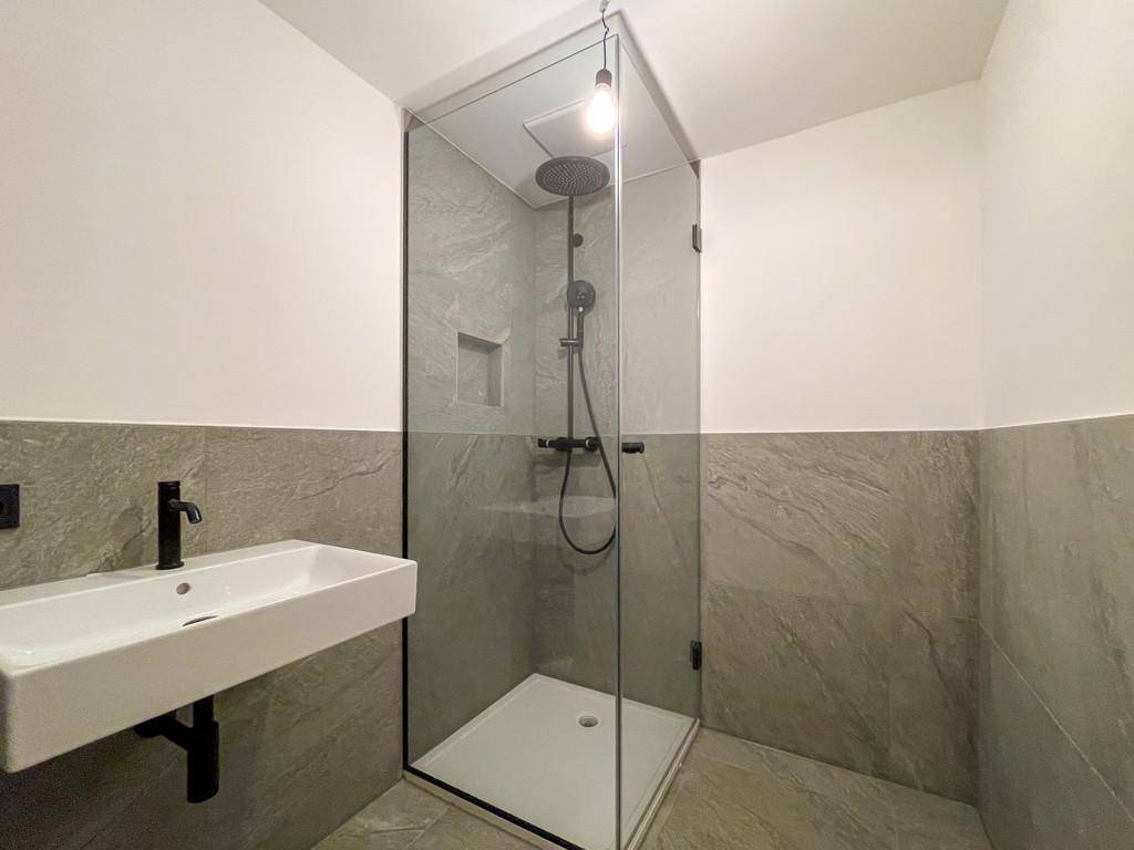 Modernes Badezimmer mit großer begehbarer Dusche, Waschbecken und grauen Fliesen.