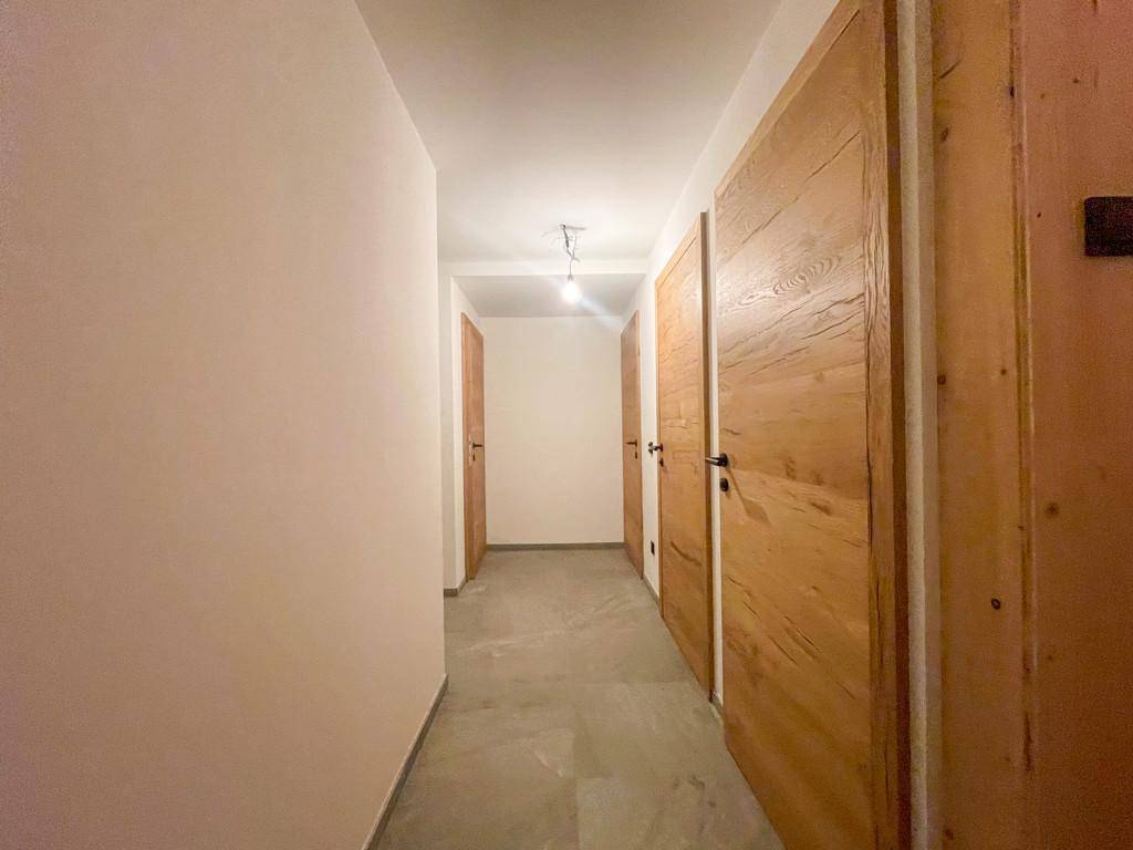 Langer Flur mit Fliesenboden und Holztüren, der zu verschiedenen Räumen führt.