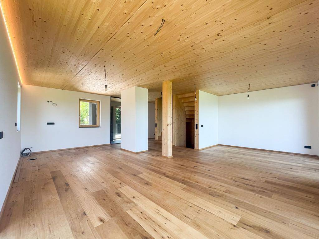 Geräumiger, heller Wohnbereich mit Holzboden und Holzdecke, bereit für individuelle Gestaltung.