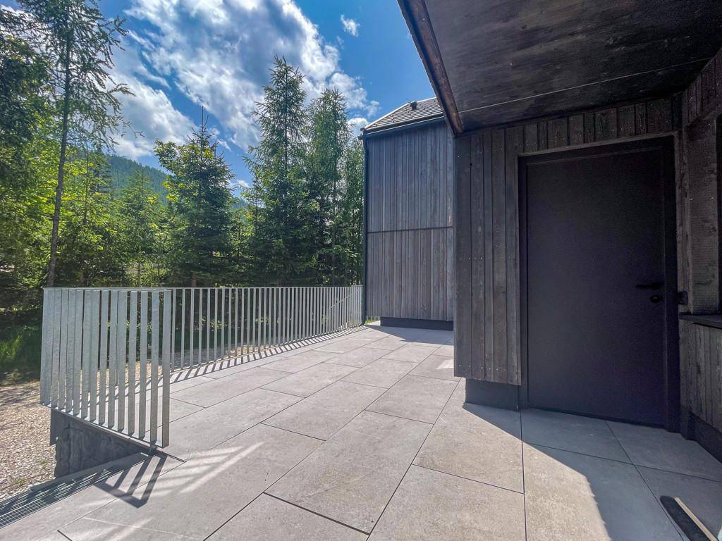 Geräumige Terrasse mit Fliesenboden und Metallgeländer, umgeben von grünen Bäumen und Natur.