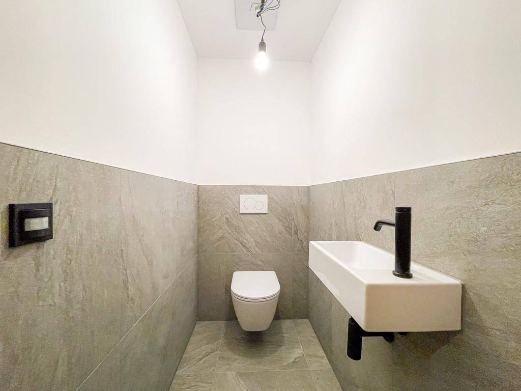 Modernes Gäste-WC mit grauen Fliesen, wandhängendem WC und kleinem Waschbecken mit schwarzer Armatur.
