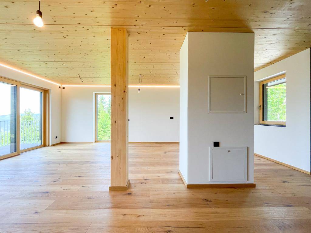 Heller Wohnbereich mit Holzboden, Holzdecke und großen Fenstern, die viel Tageslicht hereinlassen.