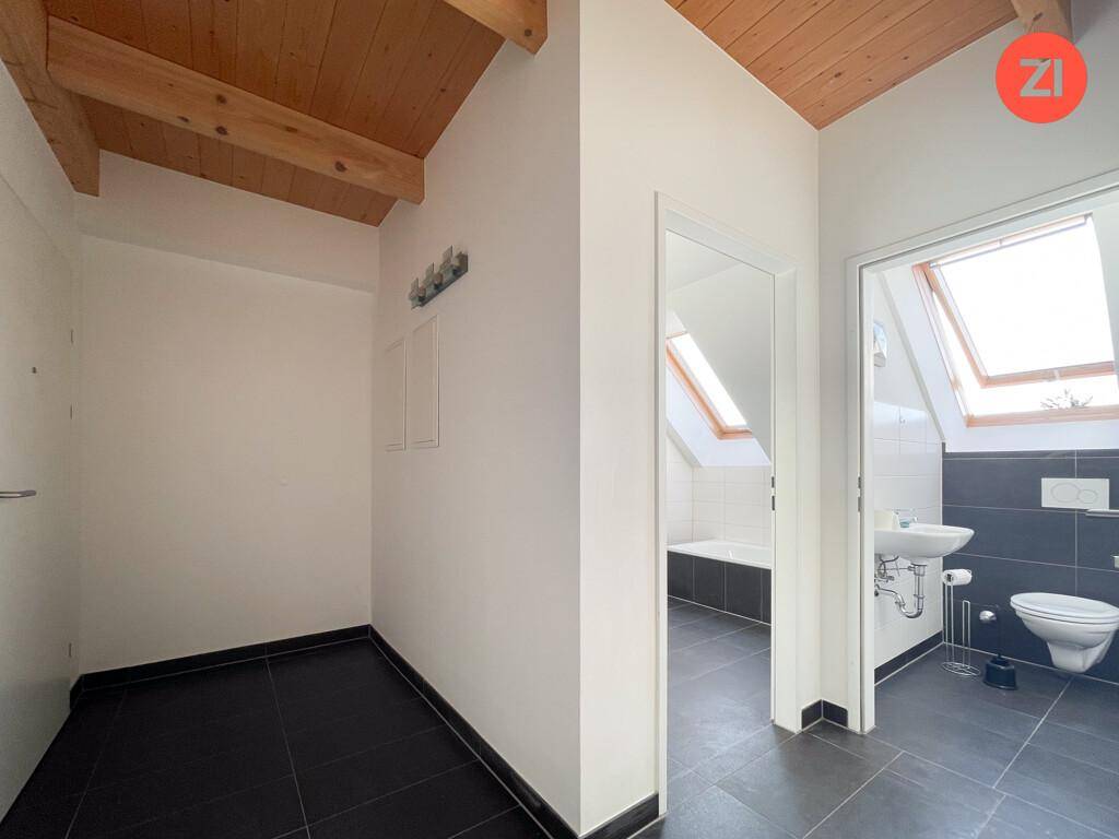 Zwei Innenansichten: ein leerer Raum mit dunklen Fliesen und ein Badezimmer mit Dachfenster.