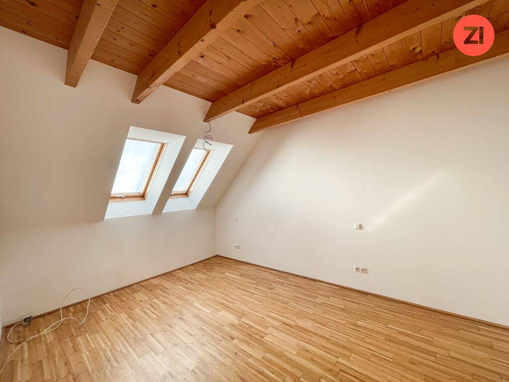 Dachgeschosszimmer mit sichtbaren Holzbalken, Parkettboden und viel Tageslicht durch die Dachfenster.