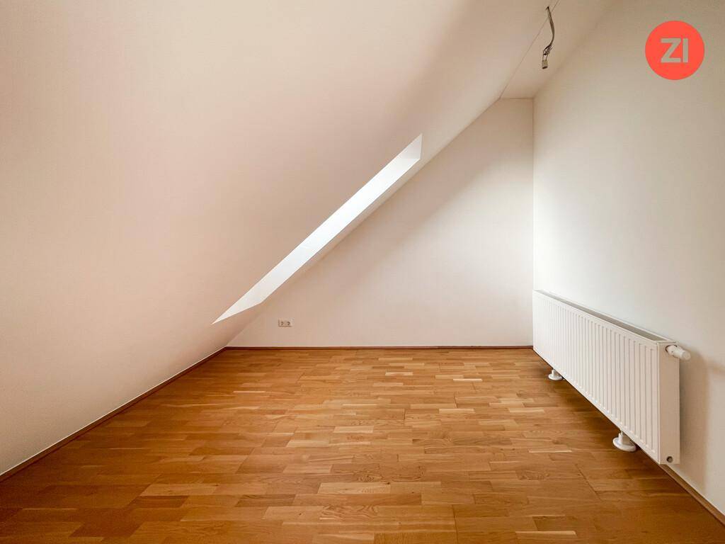 Dachgeschosszimmer mit Parkettboden, Heizkörper und schrägen Wänden, bietet gemütlichen Wohnraum.