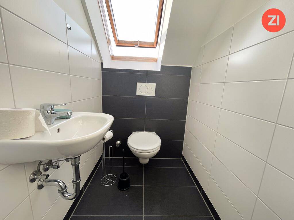 Separates WC mit dunklen Bodenfliesen, wandhängendem WC, Waschbecken und Dachfenster.