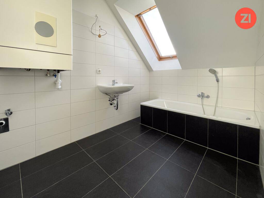 Modernes Badezimmer mit dunklen Bodenfliesen, Badewanne, Waschbecken und einem Dachfenster.