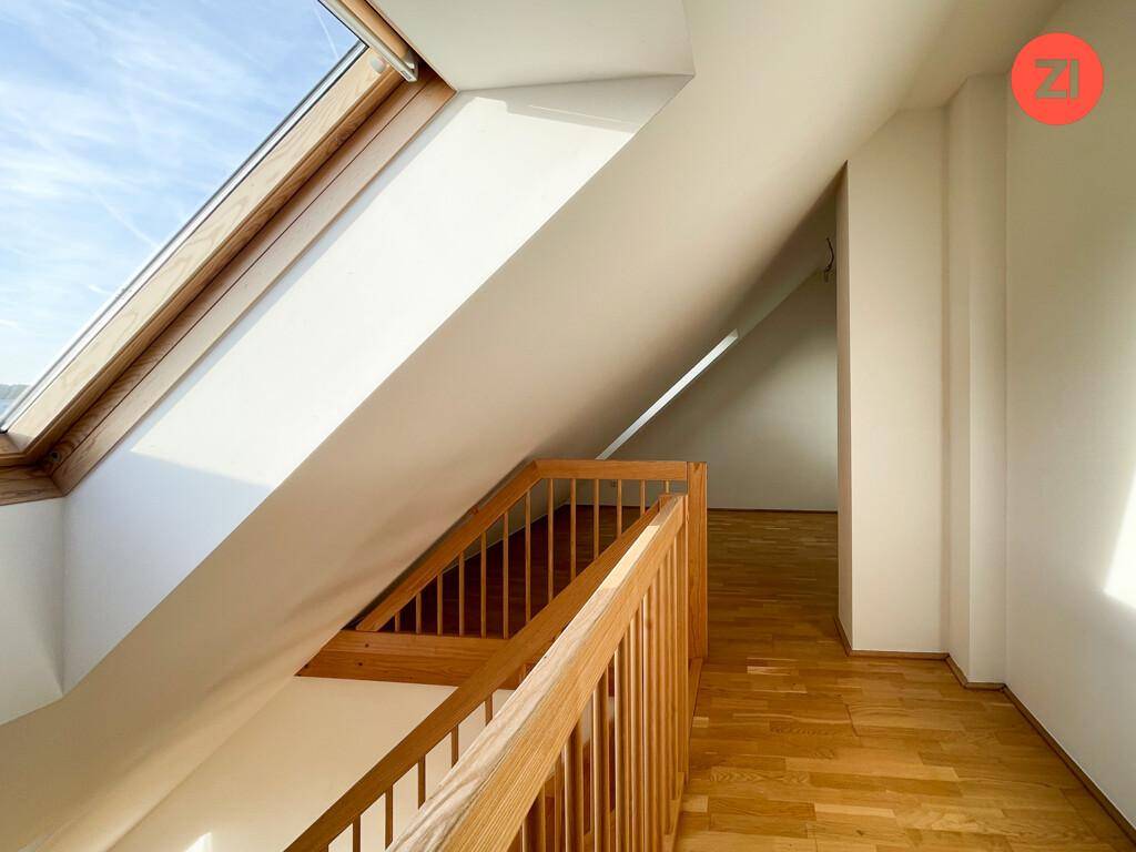 Blick vom oberen Geschoss mit Holzgeländer, Parkettboden und großem Dachfenster für viel Licht.