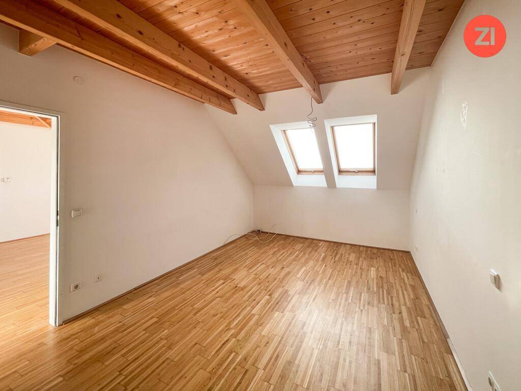 Helles Zimmer im Dachgeschoss mit Holzbalkendecke, Parkettboden und zwei Dachfenstern für viel Licht.