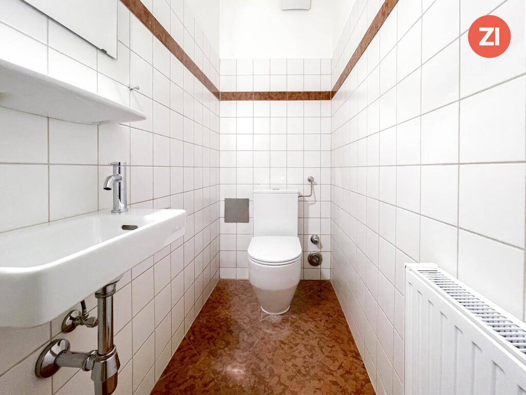 Kleines Gäste-WC mit weißen Fliesen, braunem Boden und modernem Waschbecken.