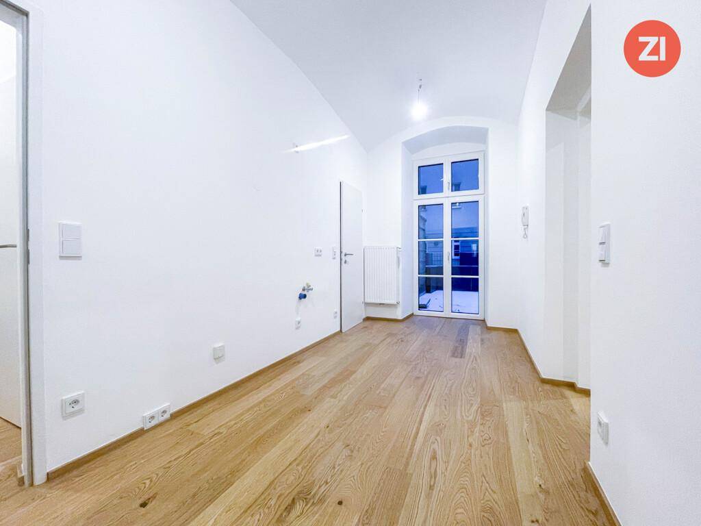 Heller Flur mit Holzboden, Fenster und Anschlüssen für eine mögliche Küchenzeile.