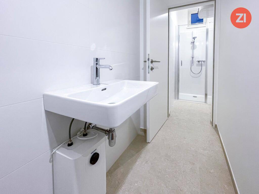 Modernes Badezimmer mit weißem Waschbecken und begehbarer Dusche im Hintergrund.