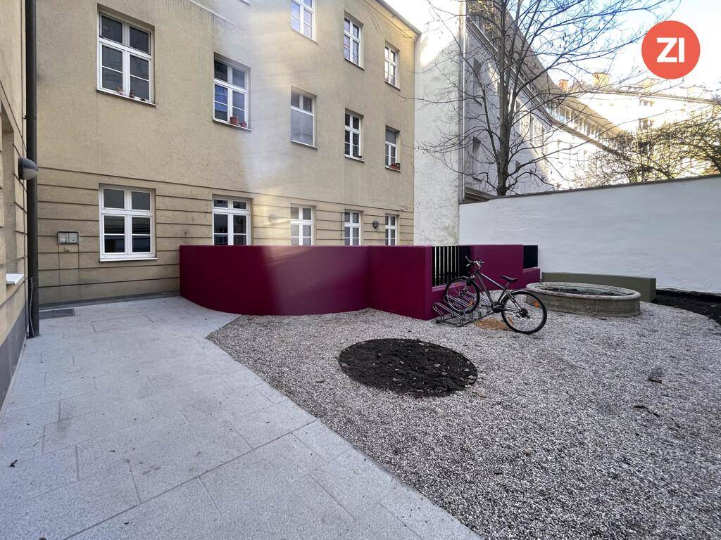 Gepflegter Hinterhof mit Kies, Fahrradabstellmöglichkeiten und einer dekorativen roten Wand.