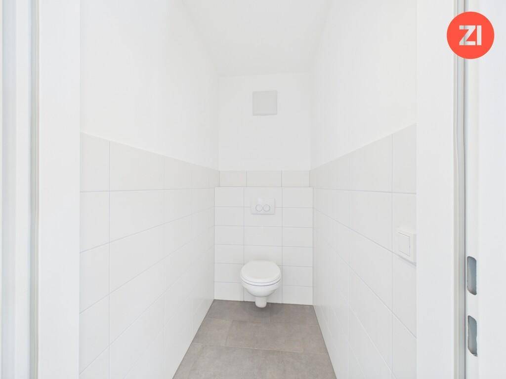 Separates WC mit wandhängender Toilette, weißen Fliesen und grauen Bodenfliesen.
