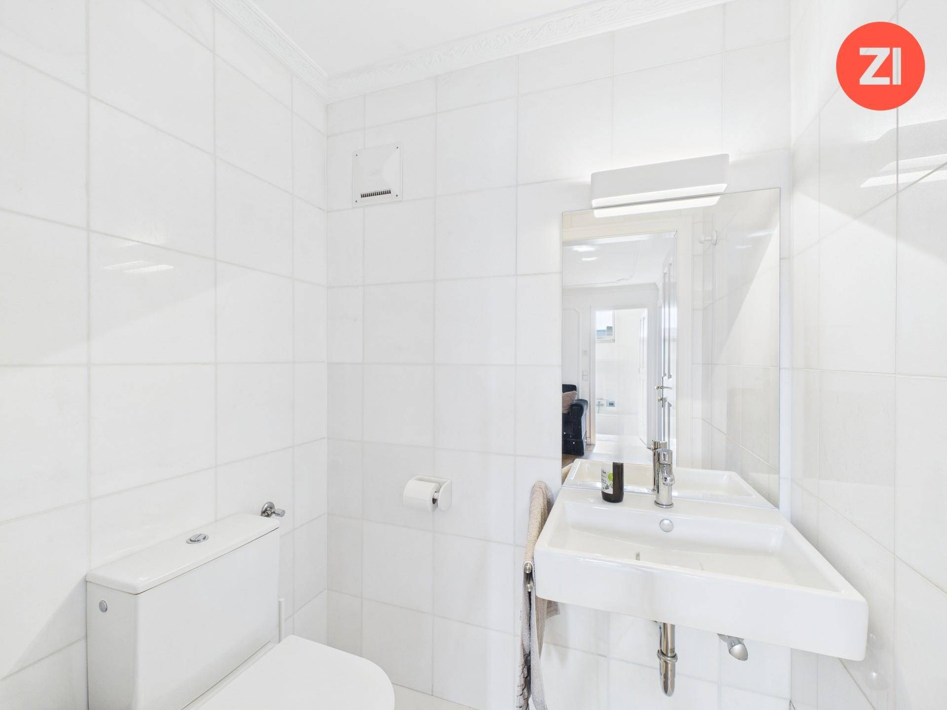 Separates WC mit Waschbecken, Spiegel und durchgehend weißen Fliesen.