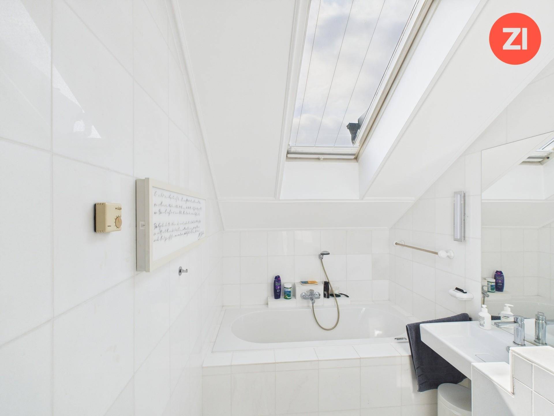Helles Badezimmer mit Badewanne, weißen Fliesen und einem Dachfenster für natürliches Licht.