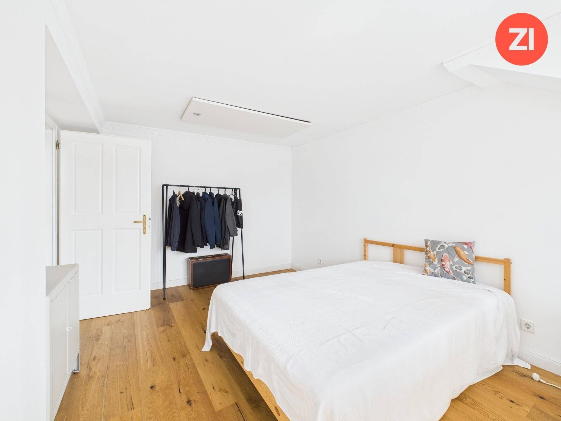 Gemütliches Schlafzimmer mit Holzboden, weiß gestrichenen Wänden und einem Kleiderständer.