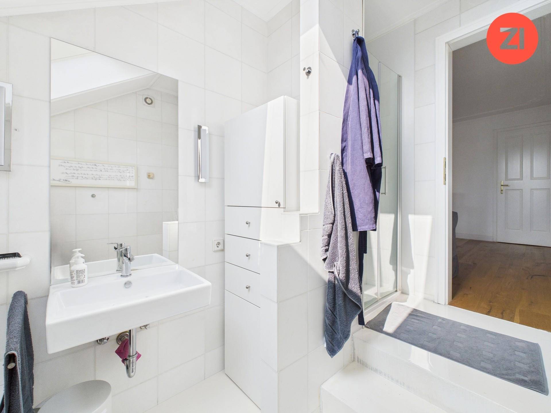 Modernes Badezimmer mit Waschbecken, Spiegel, weißen Fliesen und einer Duschkabine.