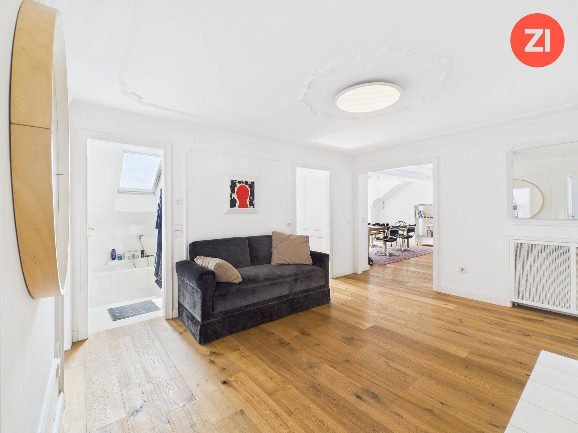 Heller Flurbereich mit Sofa, Holzboden und Zugang zu Bad und Wohnzimmer, unter einer Stuckdecke.
