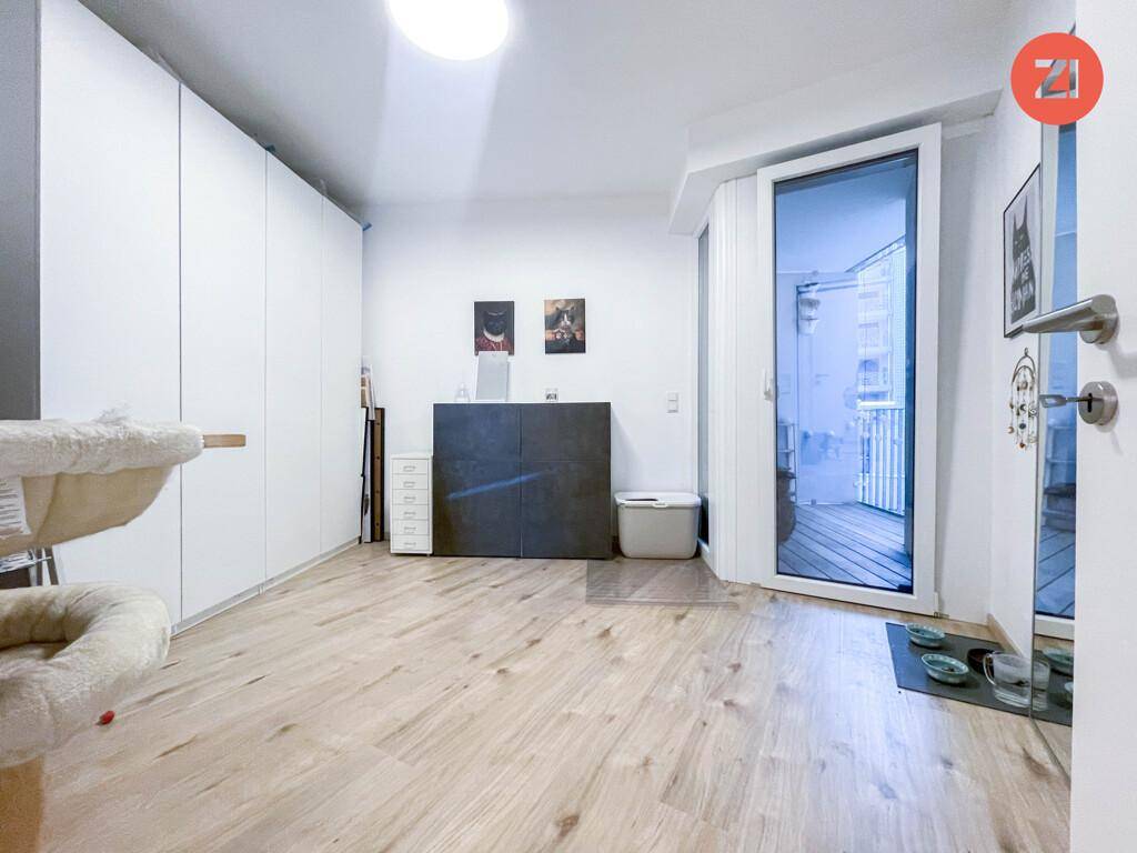 Helles Zimmer mit großem Einbauschrank, Holzboden und Zugang zu einem Balkon.