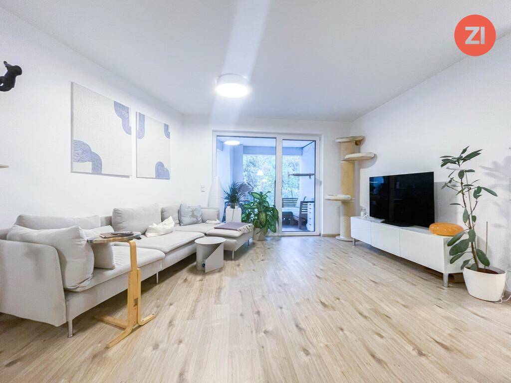 Geräumiger Wohnbereich mit hellem Holzboden, großem Sofa und Blick auf den Außenbereich.