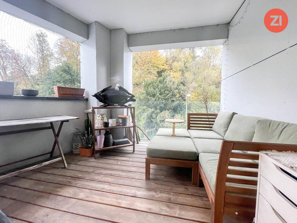 Gemütlicher Balkon mit Holzboden, Sitzgelegenheiten und Grill, umgeben von Bäumen.