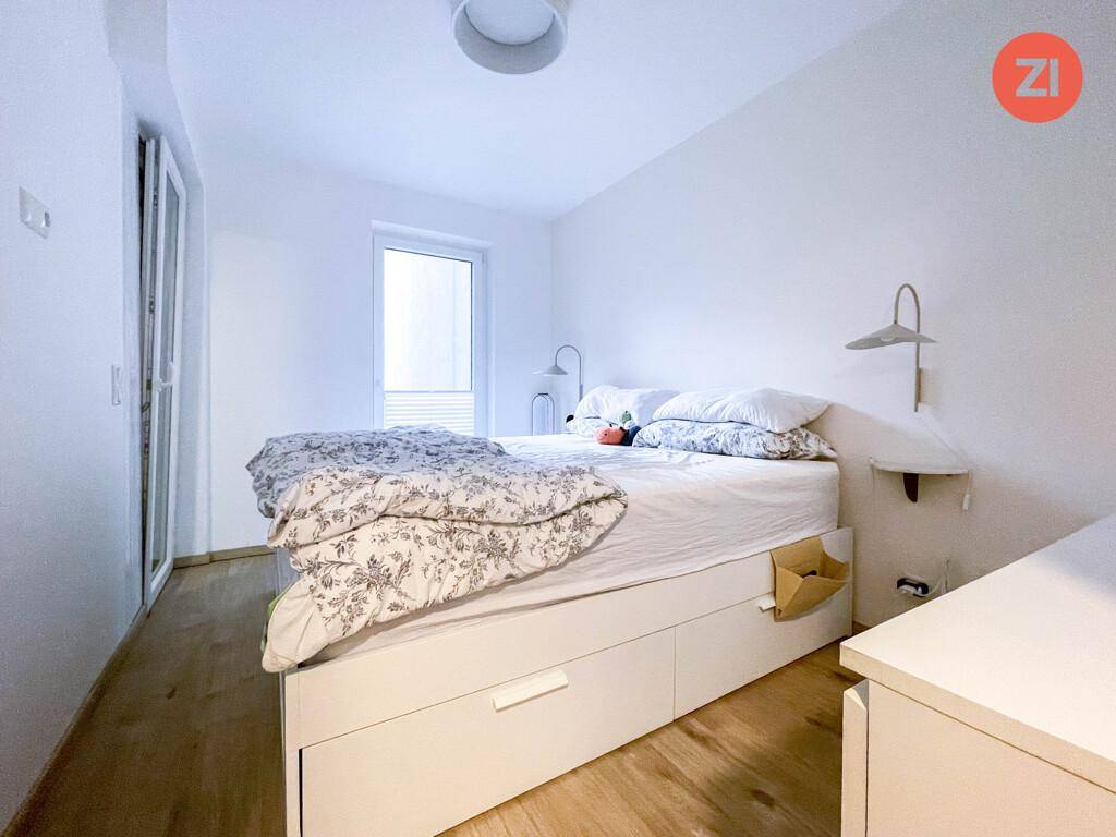 Schlafzimmer mit hellem Holzboden, weißem Bett mit Stauraum und Fenster.