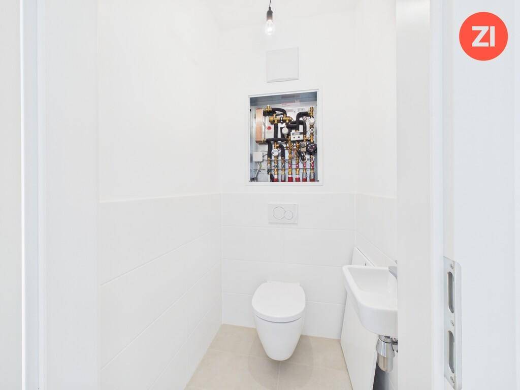 Separates WC mit wandhängender Toilette, kleinem Waschbecken und sichtbaren Installationen.