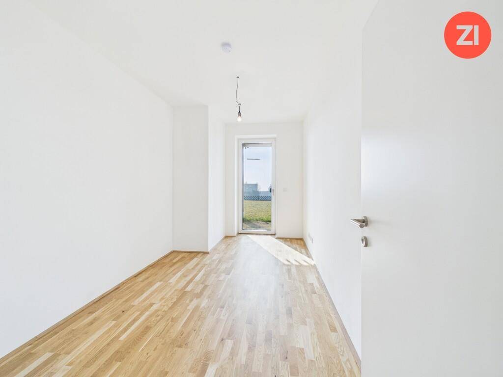 Helles Zimmer mit Holzboden und einer Tür, die ins Freie führt, ideal als Schlaf- oder Arbeitszimmer.