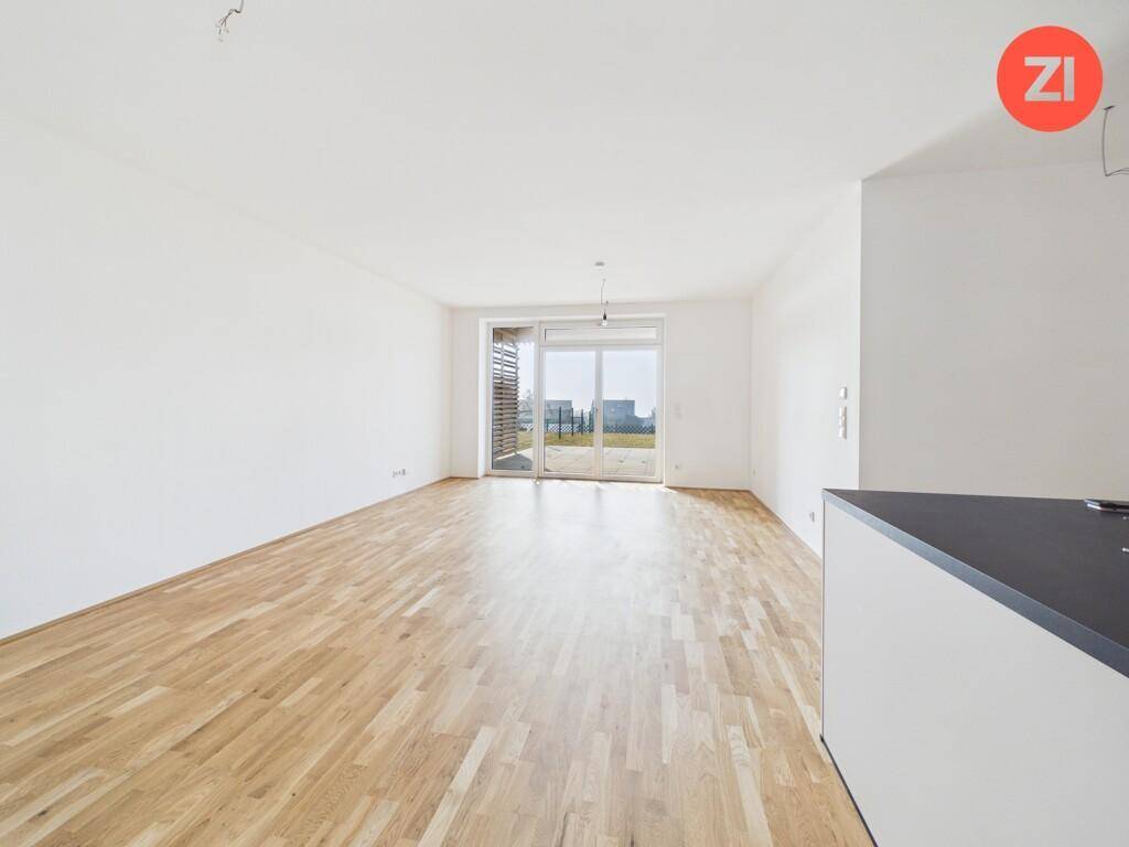 Helles, leeres Wohnzimmer mit Holzboden und großen Schiebetüren zum Außenbereich.