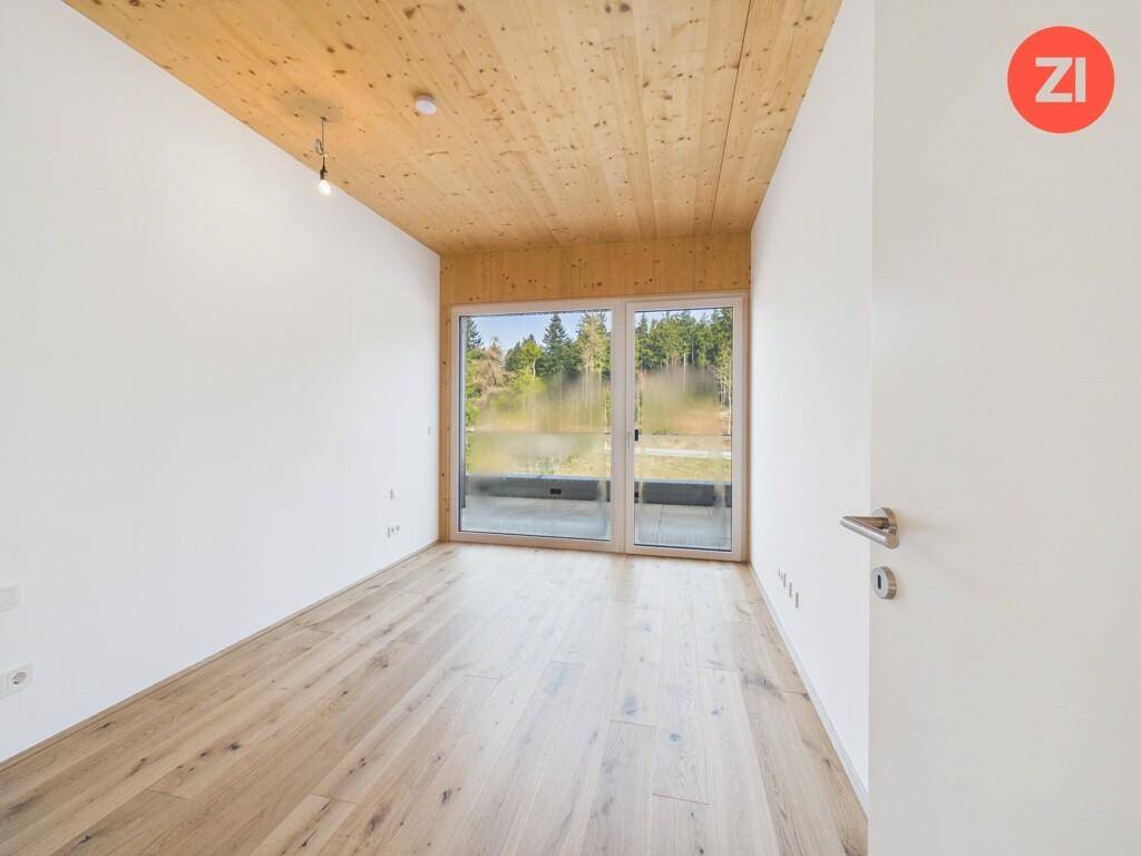 Ruhiges Zimmer mit Holzboden und Holzdecke, großen Fenstern und Blick ins Grüne.