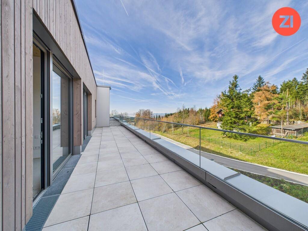 Lange, moderne Terrasse mit Fliesenboden und Glasgeländer bietet einen weiten Blick in die Natur.