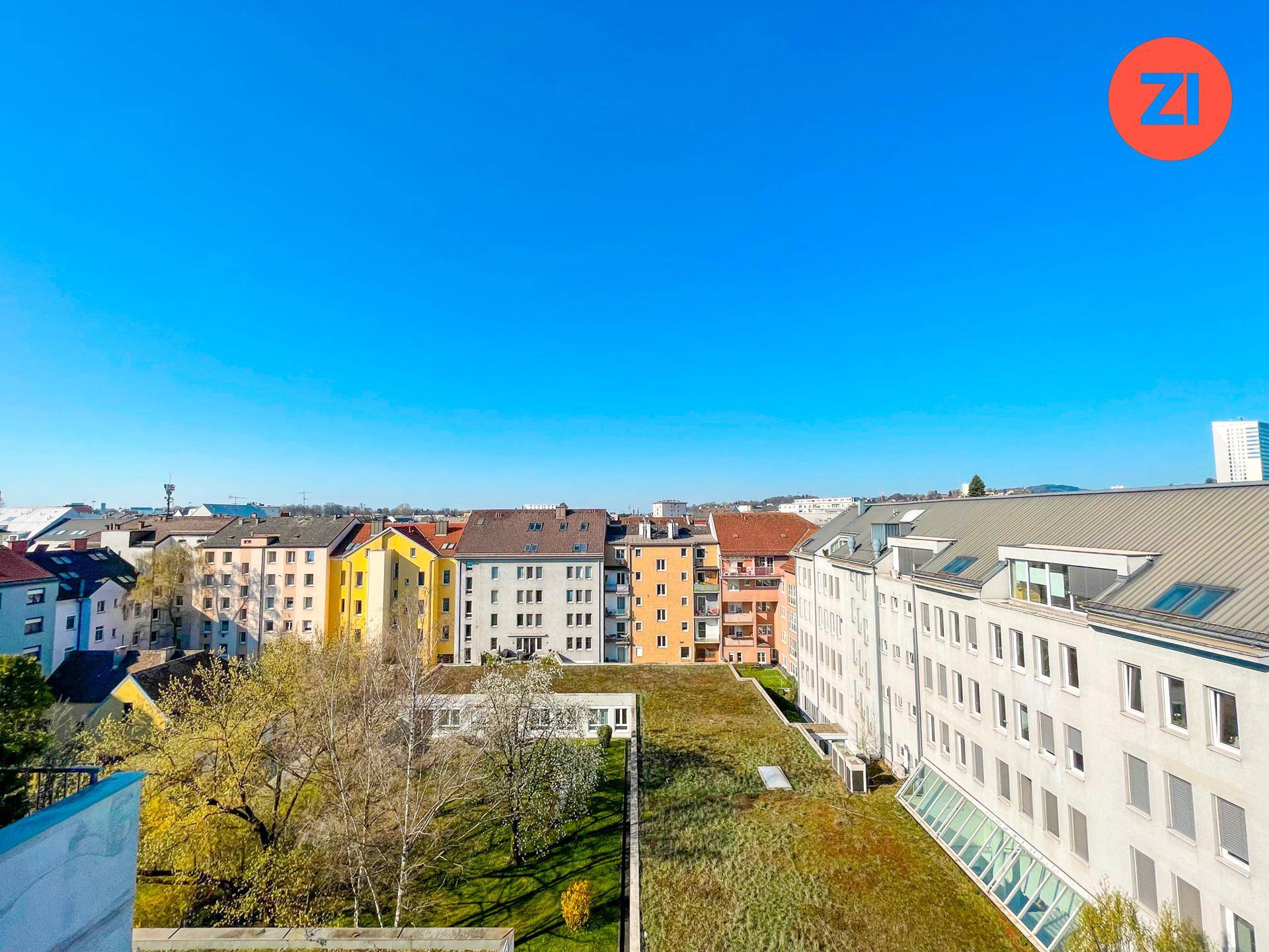 Weitläufiger Blick über die Stadt mit Wohngebäuden, begrünten Dächern und blauem Himmel.