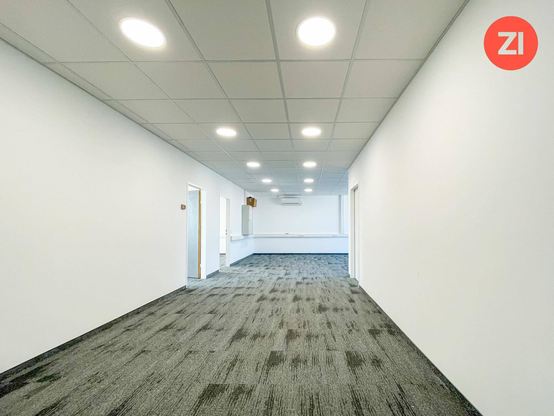 Langer, heller Bürogang mit Teppichboden, abgehängter Decke und integrierter Beleuchtung.
