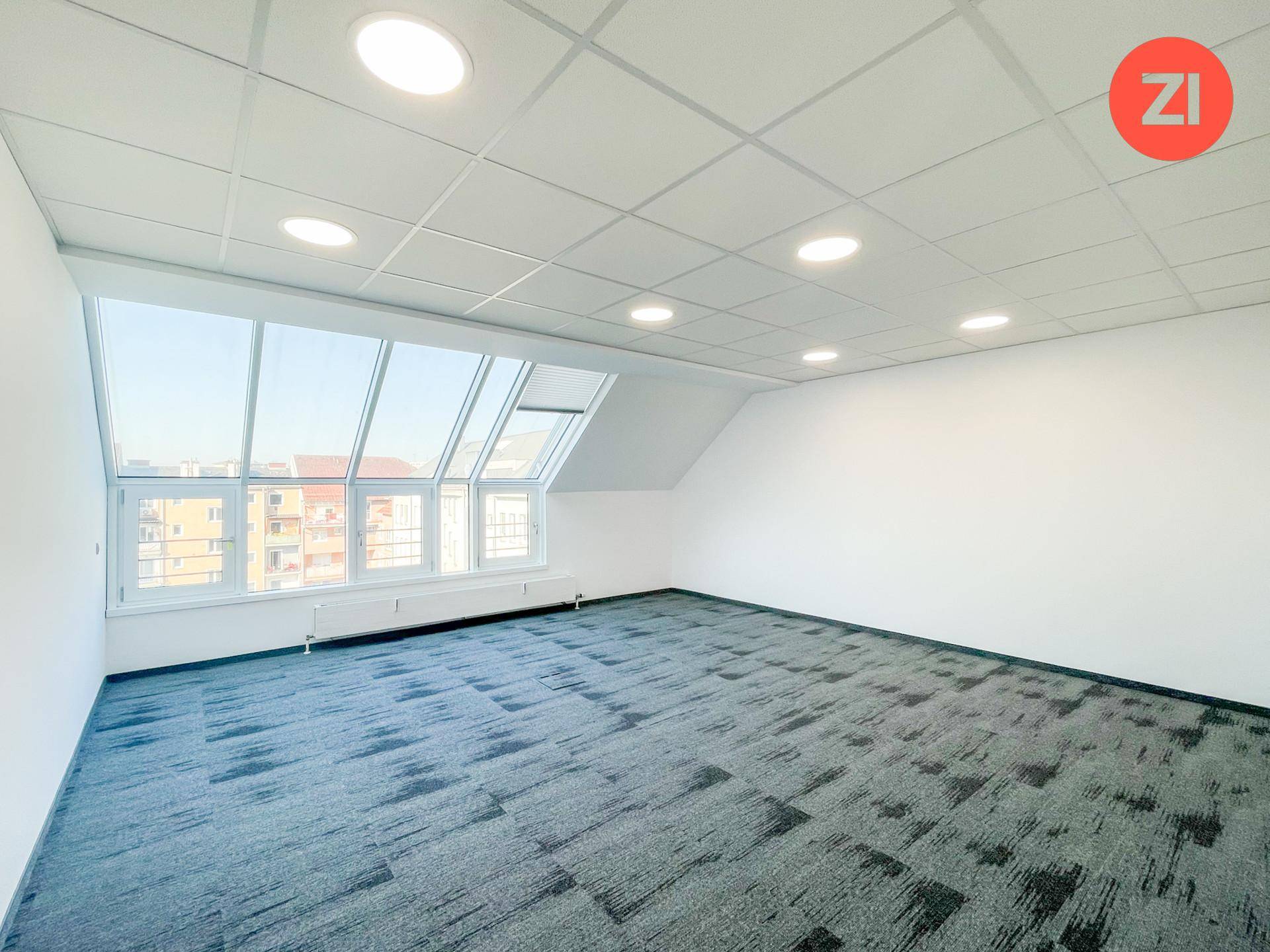Modernes Büro mit Teppichboden, abgehängter Decke und schrägen Fenstern, die viel Licht spenden.