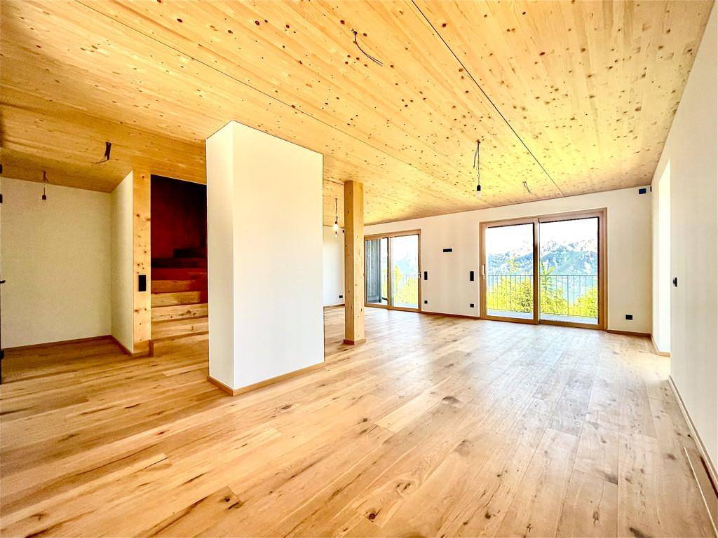 Heller, offener Wohnbereich mit Holzboden, Holzdecke und großen Schiebetüren mit Bergblick.